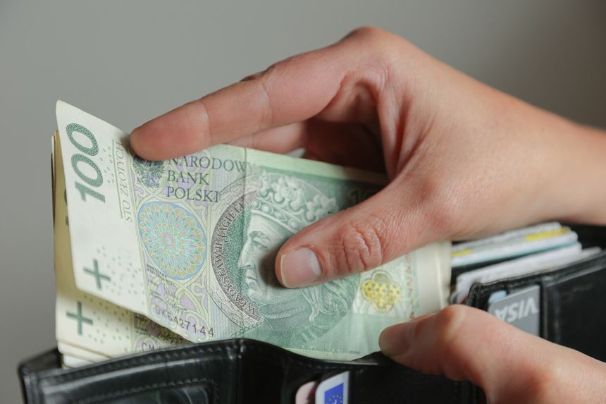 Osoba trzymająca banknot 100 zł otwiera portfel z innymi dokumentami.