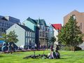 Kolorowe budynki w Reykjaviku, ludzie spacerują, na trawie odpoczywają rowerzyści.
