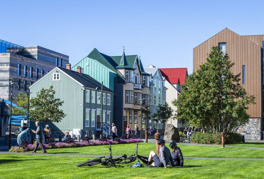 Kolorowe budynki w Reykjaviku, ludzie spacerują, na trawie odpoczywają rowerzyści.