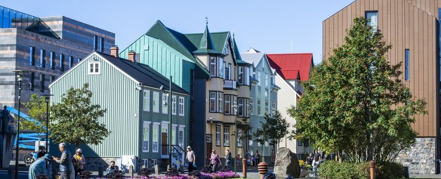 Kolorowe budynki w Reykjaviku, ludzie spacerują, na trawie odpoczywają rowerzyści.