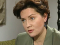 Kobieta w zielonym żakiecie, z krótkimi, kręconymi włosami, skupiona podczas rozmowy.