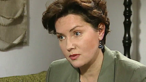 Kobieta w zielonym żakiecie, z krótkimi, kręconymi włosami, skupiona podczas rozmowy.