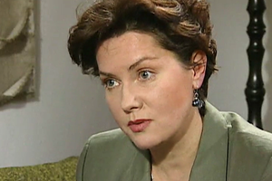 Kobieta w zielonym żakiecie, z krótkimi, kręconymi włosami, skupiona podczas rozmowy.