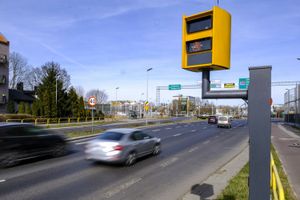 Widok ulicy z radarowym fotoradarem, oznaczeniem prędkości 40 km/h oraz poruszającymi się samochodami.