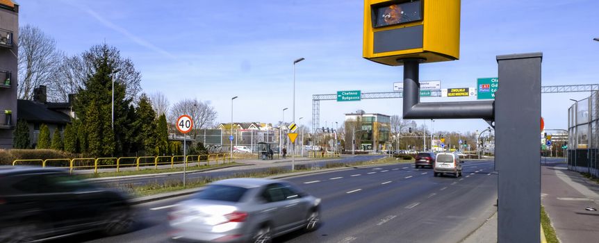 Widok ulicy z radarowym fotoradarem, oznaczeniem prędkości 40 km/h oraz poruszającymi się samochodami.