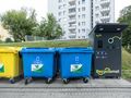 Kolorowe kontenery na odpady i automat do recyclingu w tle, w miejskim otoczeniu.