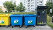 Kolorowe kontenery na odpady i automat do recyclingu w tle, w miejskim otoczeniu.