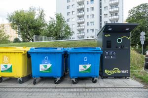 Kolorowe kontenery na odpady i automat do recyclingu w tle, w miejskim otoczeniu.