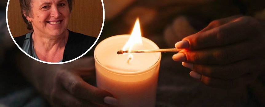 Kobieta zapala świecę, uśmiechając się. W tle przytulne, domowe otoczenie.