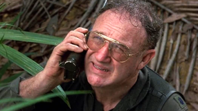 Mężczyzna w okularach, rozmawia przez telefon w gęstej dżungli. Wyraz twarzy wyraża niepokój.