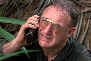 Mężczyzna w okularach, rozmawia przez telefon w gęstej dżungli. Wyraz twarzy wyraża niepokój.