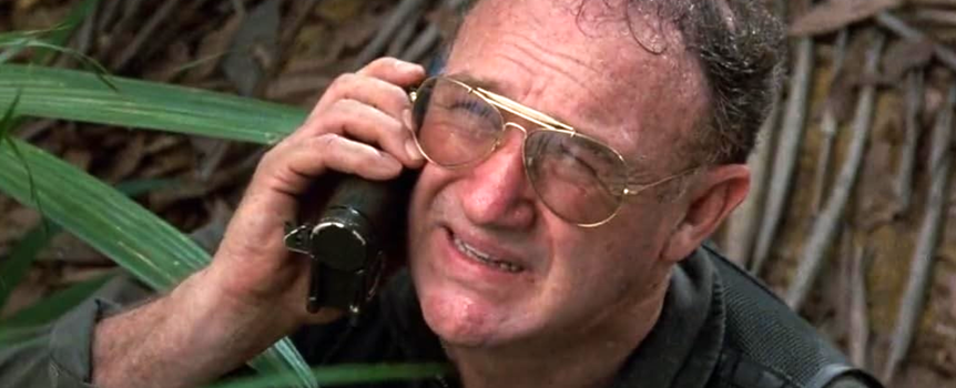 Mężczyzna w okularach, rozmawia przez telefon w gęstej dżungli. Wyraz twarzy wyraża niepokój.