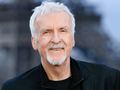 James Cameron. Mężczyzna z siwymi włosami uśmiecha się w czarnym ubraniu.