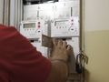 Mężczyzna w czerwonej koszulce obsługuje licznik energii elektrycznej. W tle widoczne dwa liczniki.