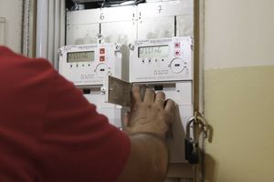 Mężczyzna w czerwonej koszulce obsługuje licznik energii elektrycznej. W tle widoczne dwa liczniki.