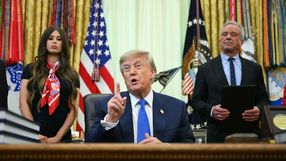 Na zdjęciu Donald Trump, przemawiający przy biurku, z kobietą i mężczyzną w tle.