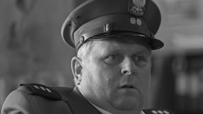 Mężczyzna w mundurze policjanta, z zaskoczoną miną, patrzy w dal. Czarno-biała fotografia.