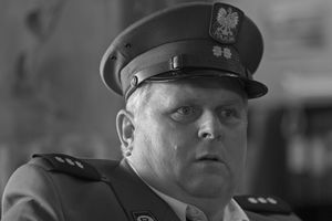 Mężczyzna w mundurze policjanta, z zaskoczoną miną, patrzy w dal. Czarno-biała fotografia.