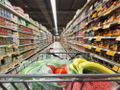 Zakupy w supermarkecie: wózek z warzywami i owocami na tle regałów pełnych produktów.