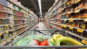 Zakupy w supermarkecie: wózek z warzywami i owocami na tle regałów pełnych produktów.