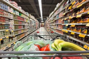 Zakupy w supermarkecie: wózek z warzywami i owocami na tle regałów pełnych produktów.