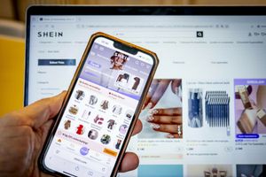 Zbliżenie na telefon trzymany w dłoni z aplikacją SHEIN i strony internetowej na laptopie.