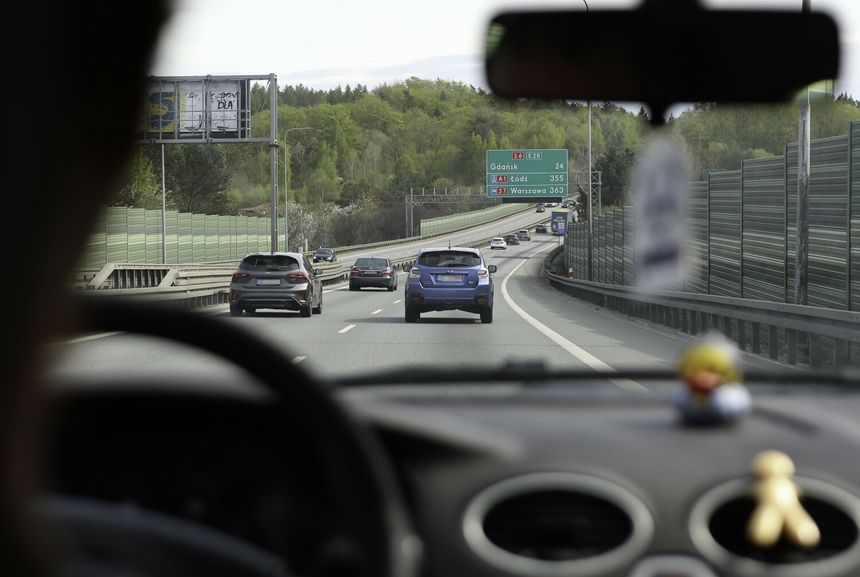 Widok z wnętrza samochodu na autostradę z znakami kierunkowymi do Gdańska i Łodzi.