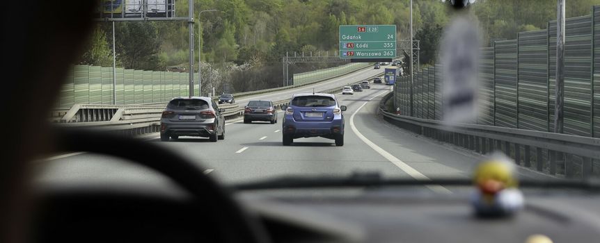 Widok z wnętrza samochodu na autostradę z znakami kierunkowymi do Gdańska i Łodzi.