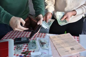 Dwie osoby wymieniają pieniądze przy stole, obok kalkulator, dokumenty i monety.