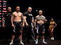 Mężczyźni w sportowych strojach na scenie, z kobietą w tle. Atmosfera sportowa.