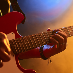 Zbliżenie na ręce grające na czerwonej gitarze elektrycznej w kolorowym świetle.