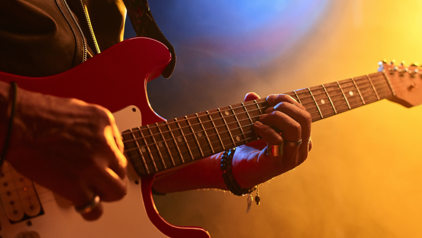 Zbliżenie na ręce grające na czerwonej gitarze elektrycznej w kolorowym świetle.