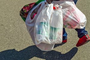 Osoba niesie kilka pełnych toreb plastikowych na chodniku. Widać czerwone buty.