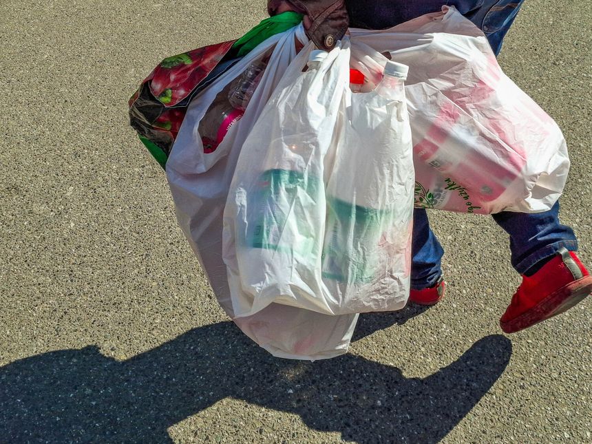 Osoba niesie kilka pełnych toreb plastikowych na chodniku. Widać czerwone buty.