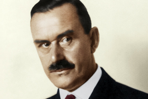 Mężczyzna w eleganckim garniturze, o ciemnych włosach i wąsach, patrzy w bok.