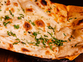 Puszysty chleb naan posypany świeżą kolendrą, podany na talerzu.