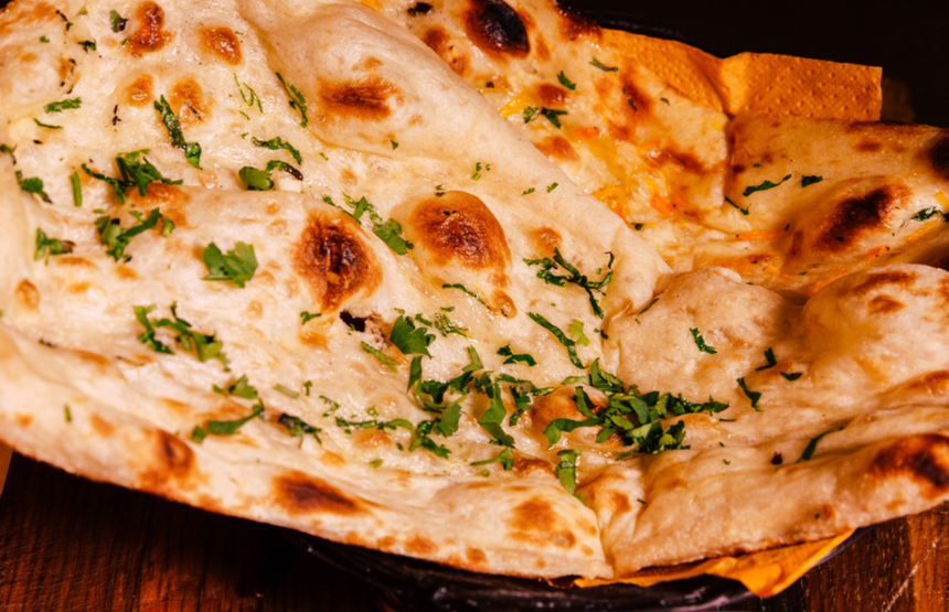 Puszysty chleb naan posypany świeżą kolendrą, podany na talerzu.