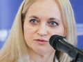 Portret kobiety z jasnymi włosami, przy mikrofonie, w tle niebieska ściana.