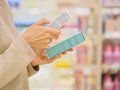 Osoba trzymająca dwie butelki kosmetyków w sklepie, na tle kolorowych produktów.