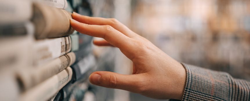Zdjęcie przedstawia dłoń dotykającą książek na półce w bibliotece.