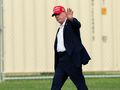 Mężczyzna w czapce z napisem „Make America Great Again” macha ręką. Ubrany w garnitur i koszulę.