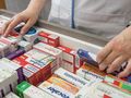 Osoba w białym fartuchu rozkłada leki w aptece, dostosowując je do porządku.