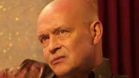 Mężczyzna z krótkimi włosami, poważnym wyrazem twarzy, na tle kolorowej ścianki.