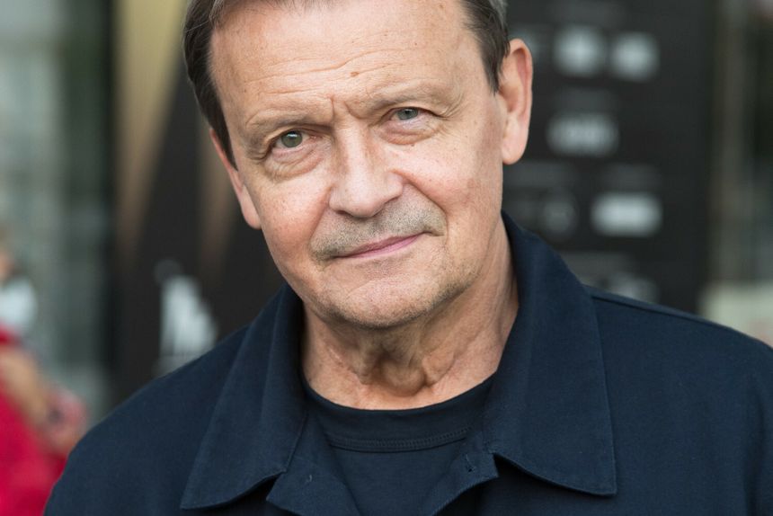 Zdjęcie mężczyzny w granatowej kurtce, uśmiechającego się, na tle jasnego tła.