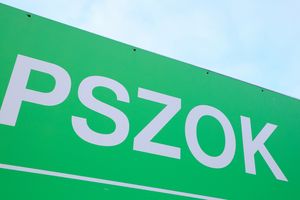 Zielony znak z białymi literami „PSZOK” na tle nieba. Brak widocznych ludzi.