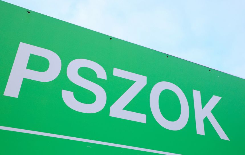 Zielony znak z białymi literami „PSZOK” na tle nieba. Brak widocznych ludzi.