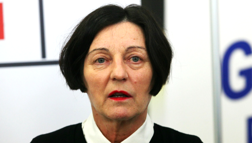 Kobieta o krótkich, ciemnych włosach w czarnej bluzce i białej koszuli, z czerwonymi ustami.