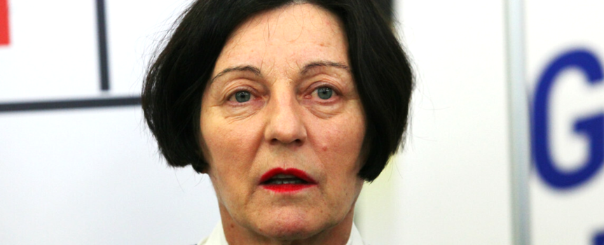 Kobieta o krótkich, ciemnych włosach w czarnej bluzce i białej koszuli, z czerwonymi ustami.
