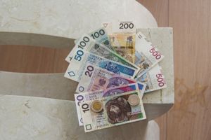 Na zdjęciu plik polskich banknotów o różnych nominałach ułożony na kamiennej powierzchni.