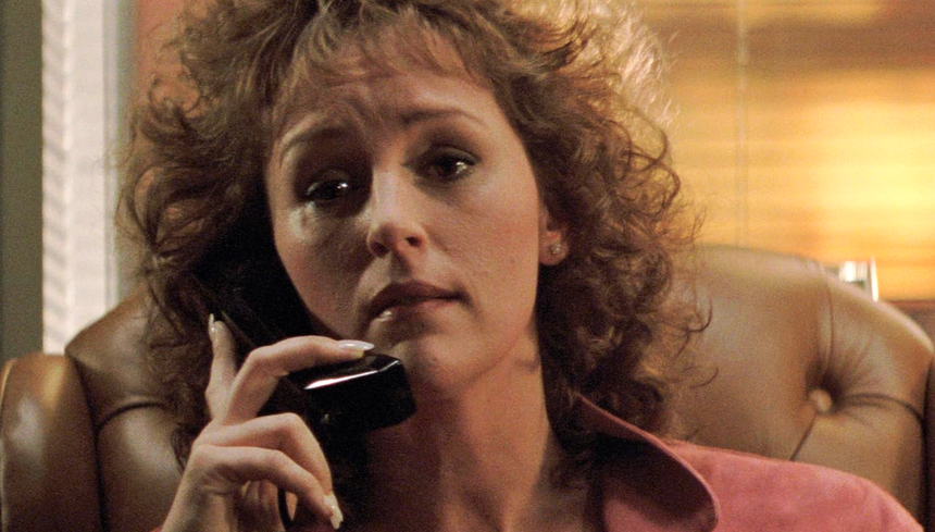 Kobieta o kręconych włosach, rozmawia przez telefon w biurze, wyraz twarzy skupiony.